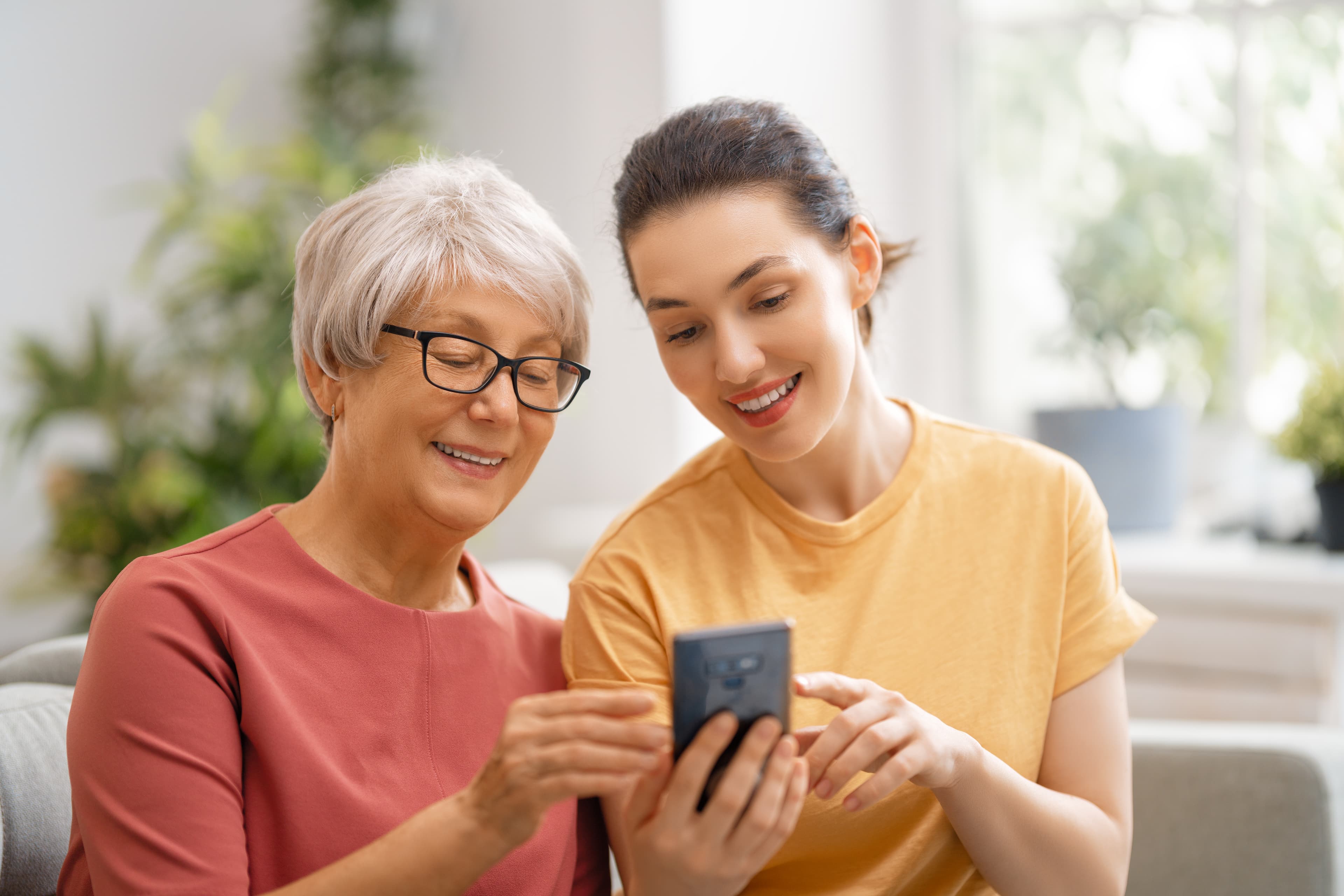Older mother and adult daughter sitting together and looking at a smartphone.